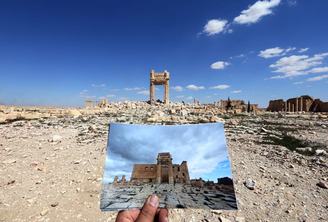A photographer holds his March 2014 picture of the Temple of Bel in front of the remains of the historic temple on 31 March 2016.