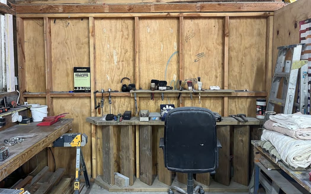 A desk and workbench inside Gloriavale's paint shop. Tools, paint brushes and folded drop cloths are present across the surfaces, including the wall.
