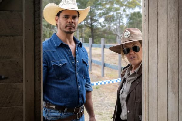 A woman dressed as a detective and a man wearing a cowboy hat look through a door.