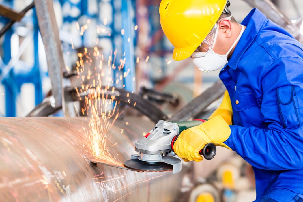 Industrial worker in manufacturing plant grinding to finish a pipeline.
