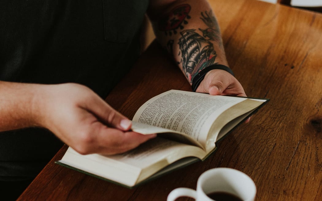 Man with tattoos reading and drinking coffee