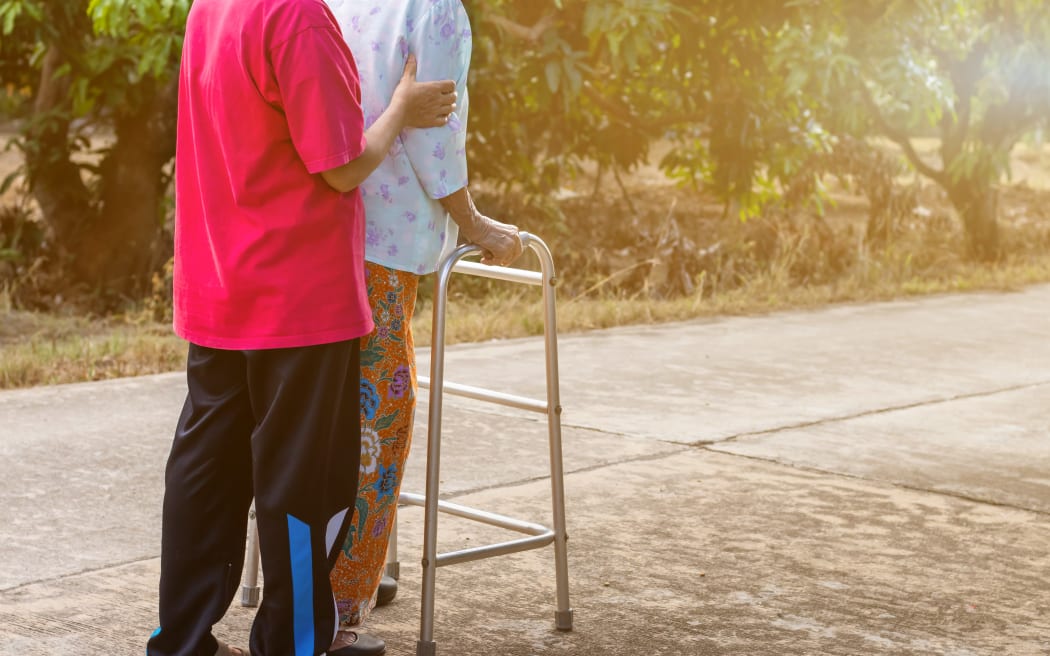 Asian old woman standing with her hands on a walker with daughter's hand,Hand of old woman holding a staff cane for helping walking