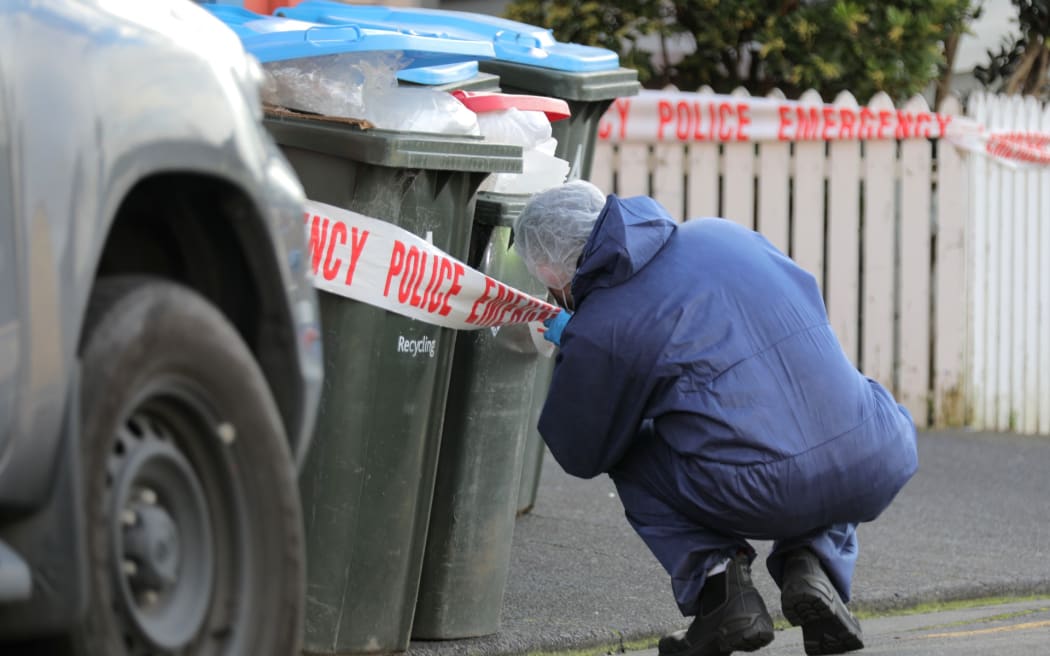 A police investigator looks closely at a set of rubbish bins on Renall St