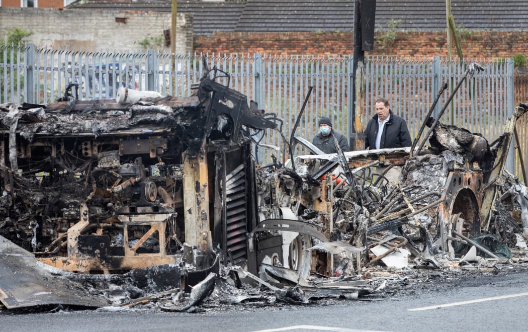 Members of the public walk past the remains of a burnt out bus on the loyalist Shankill Road in Belfast, after it was set on fire during a night of violence on April 8, 2021.