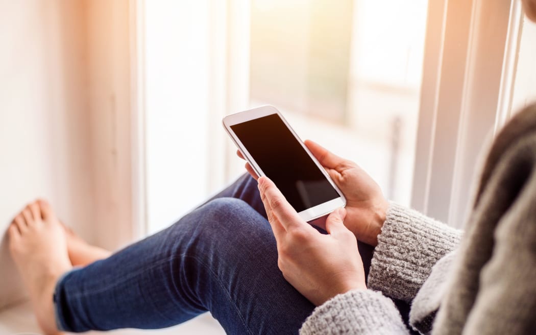 woman sitting on window sill with smart phone