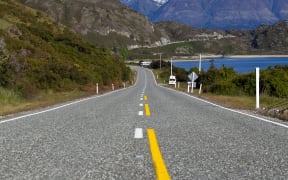 An empty stretch of road in New Zealand's South Island, with mountains and a lake in the background