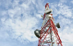 Tower with cell phone antenna system against blue sky.