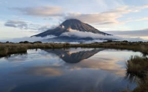Mount Taranaki is reflected in a tarn on the Pouakai Crossing