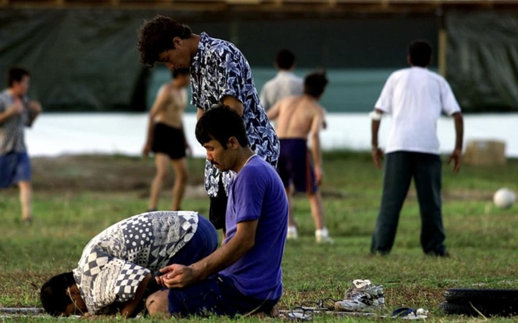 A small group of Muslim refugees pray at sunset while other refugees participate in a football match at a camp for the asylum seekers on Nauru, 20 September 2001. The first of hundreds of mainly Afghan refugees arrived on the island 19 September from the Australian troopship Manoora.