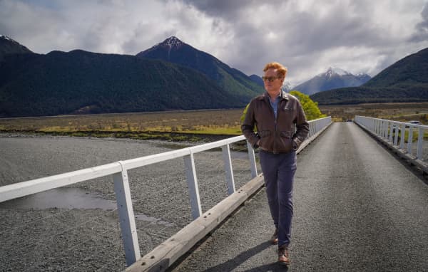 American TV host and comedian Conan O'Brien walks across a bridge in New Zealand while filming for his travel show Conan O’Brien Must Go in 2024.
