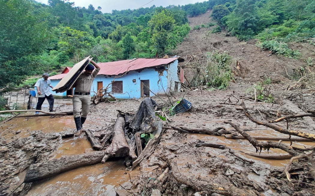 A security personnel carries the belongings of a villager from the site of a landslide after heavy rains at Jadon village in Solan district of India's Himachal Pradesh state on 14 August 2023. At least 16 people have been killed, nine of them in a temple collapse, and dozens more are feared missing after intense rains caused floods and landslides in India, officials said.