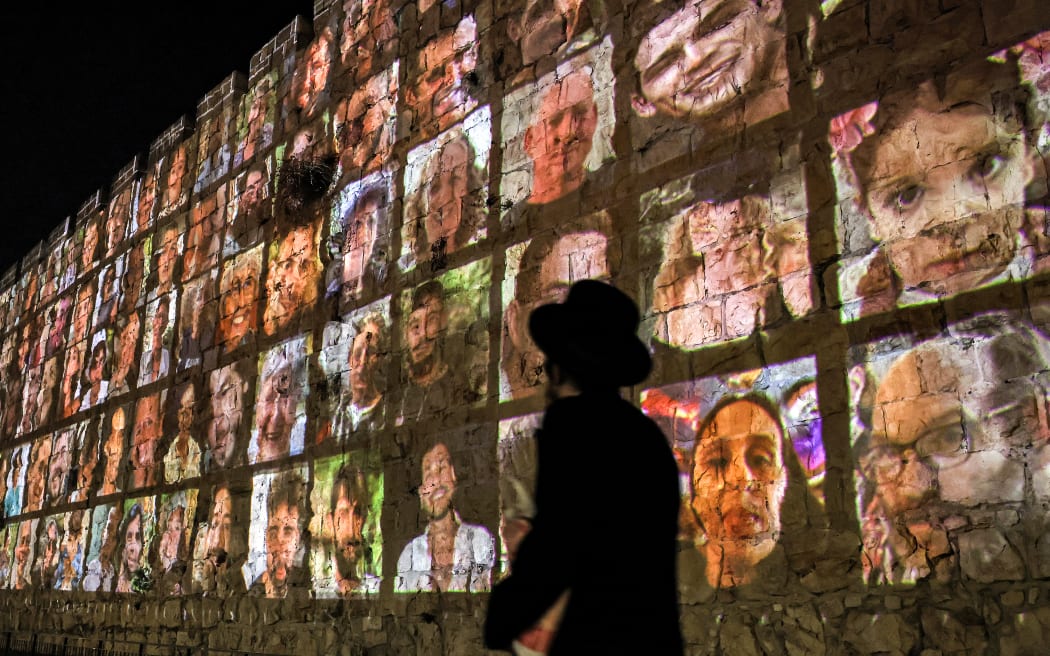 An Jewish man walks outside the walls of the old city of Jerusalem, on which are projected pictures of the hostages abducted by Palestinian militants on the October 7 attack and currently held in the Gaza Strip, on November 6, 2023, amid the ongoing battles between Israel and the militant group Hamas. (Photo by AHMAD GHARABLI / AFP)