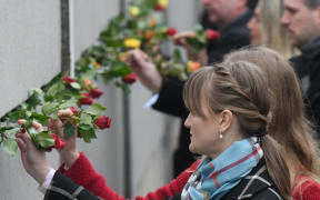 People place roses at a portion of the wall at Bernauer Strasse during a commemoration ceremony for the 30th anniversary of the fall of the Berlin Wall, at the Berlin Wall Memorial, Bernauer Strasse in Berlin.