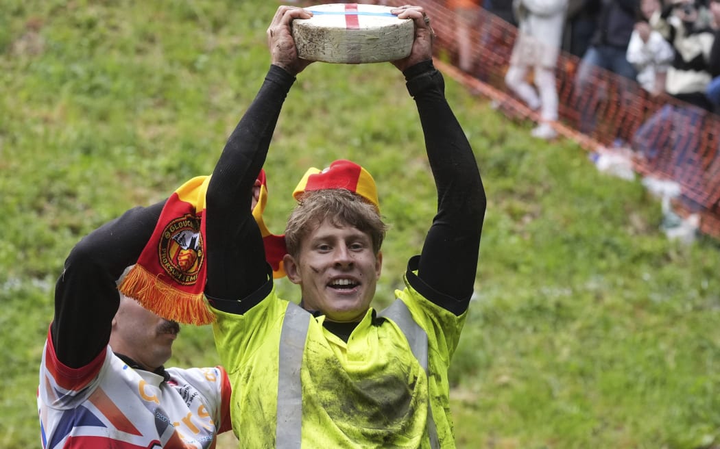 Tom Kopke, from Munich, winner of the first race, lifts a Double Gloucester cheese after taking part in the annual cheese rolling at Cooper's Hill in Brockworth, England, Monday, May 27, 2024. The traditional event attracts people from around the globe who come to chase a 7lb Double Gloucester cheese down the steep Coopers Hill. (Jacob King/PA via AP)