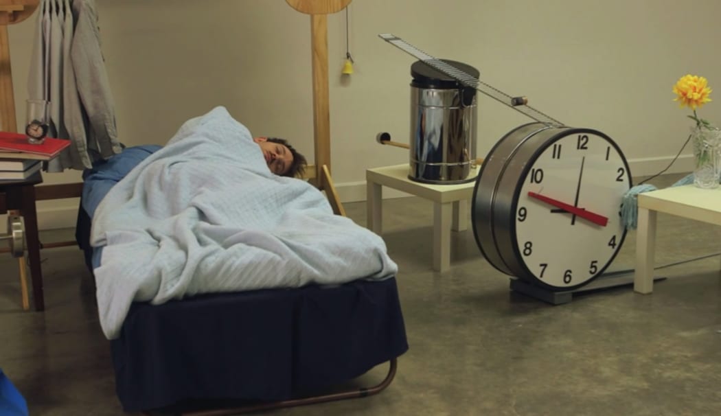 A still from the documentary, 'Joseph Gets Dressed' showing Joseph Herscher lying in bed surrounded by the machine that will wake him and dress him.