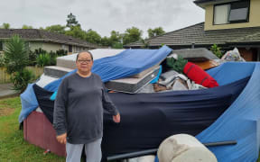 Māngere resident Pauline Ekieleu standing next to a skip bin full of furniture that was ruined by floodwaters and is now set for the dump.