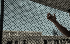 A hand holds onto the wire in prison