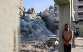 A man takes cover behind a column as an explosion propagates smoke and dust during an Israeli strike which reportedly targeted a school in the Zeitoun district on the outskirts of Gaza City, on September 1, 2024, amid the ongoing conflict between Israel and the Palestinian Hamas group. (Photo by Omar AL-QATTAA / AFP)