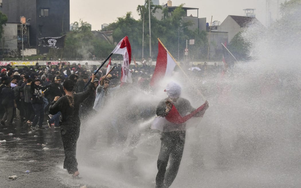 Students throw objects at the police while being sprayed with a water cannon during a protest outside the parliament building against lawmakers’ demands for higher allowances in Jakarta on August 28, 2025. (Photo by BAY ISMOYO / AFP)