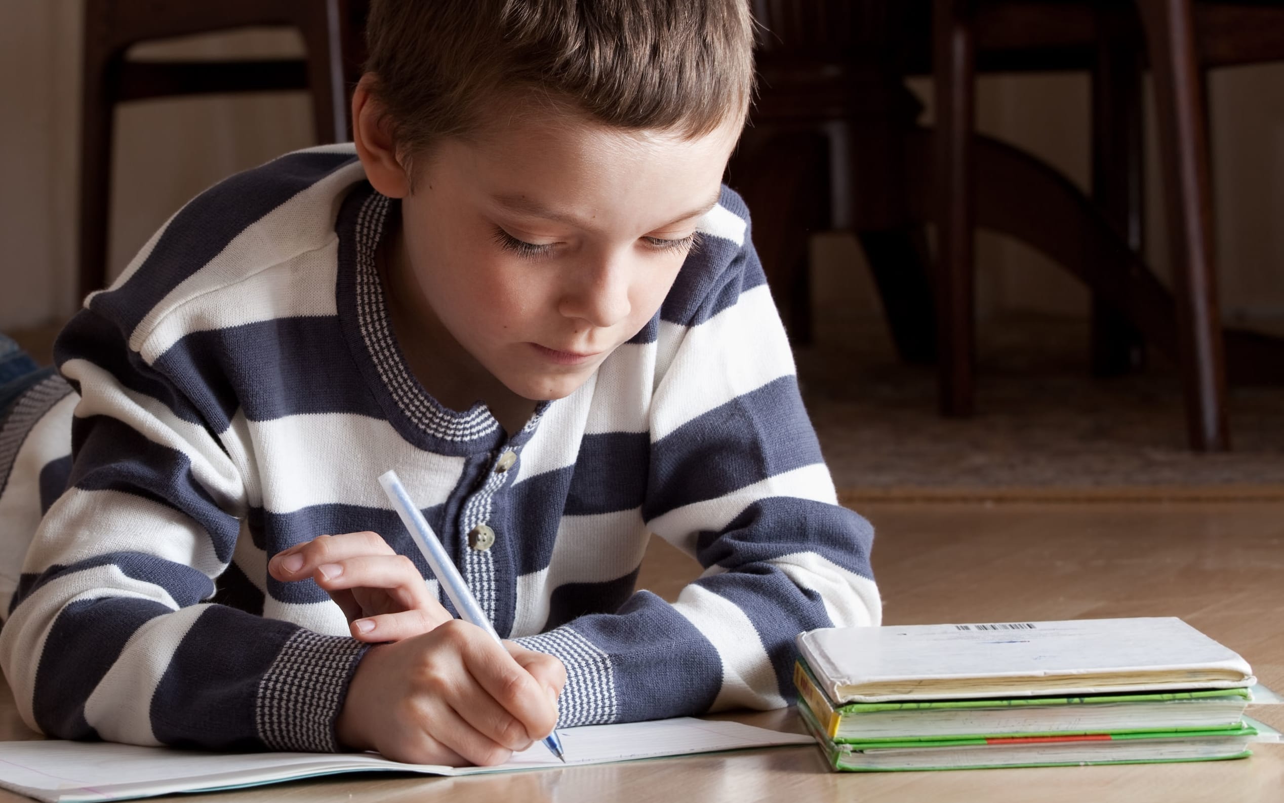 A primary school student does his homework on the floor at home.