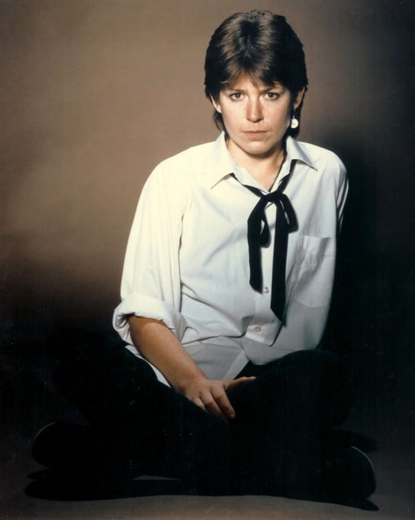 Shona Laing wears a white shirt, and black tie and stares down the camera.