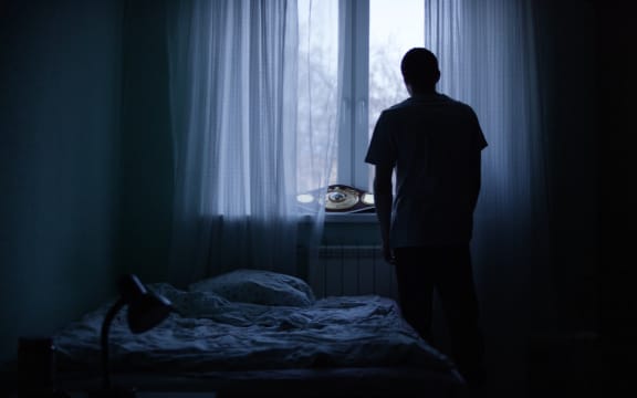 Alone man silhouette staring at the window closed with curtains in bedroom.