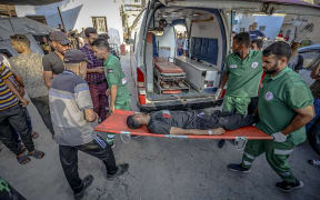 Medics carry a wounded man as a person killed and several wounded as as a result of Israel's targeting of the Al-Rifai family home on the edge of the tunnel east of Gaza City arrive at the Baptist Hospital on July 15, 2025.