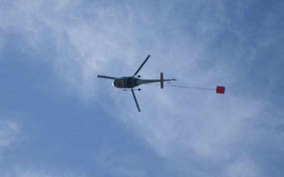 A helicopter with a monsoon bucket fights a fire at Arthur's Pass.