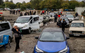 People walk between cars damaged by a missile strike on a road near Zaporizhzhia on September 30, 2022.