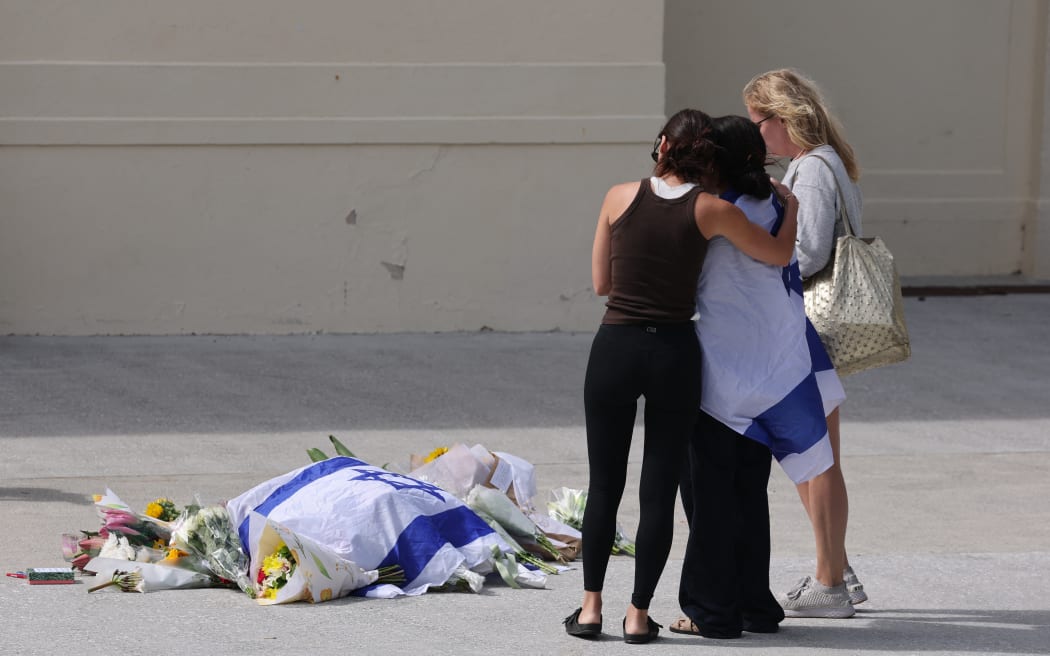 People look at flowers in front of the Bondi Pavillion laid in memory of the victims of a shooting at Bondi Beach in Sydney on December 15, 2025. A father-and-son team toting long-barrelled guns shot and killed 15 people including a 10-year-old girl at Sydney's Bondi Beach, authorities said on December 15, labelling it an antisemitic terrorist attack on a Jewish festival. (Photo by DAVID GRAY / AFP)