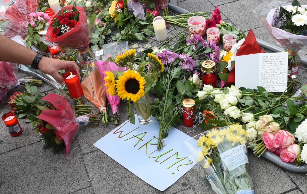 A candle is placed next to a sign reading "Why" and flowers laid down for the victims of the shooting.