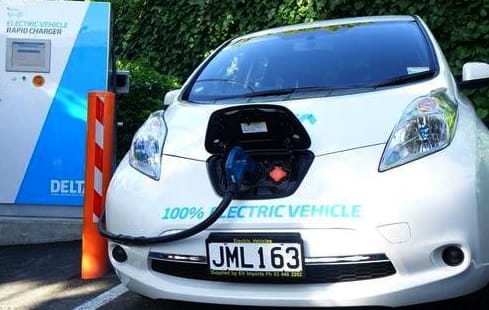 An a white electric car with a black cable running into the bonnet at a charging station, Dunedin