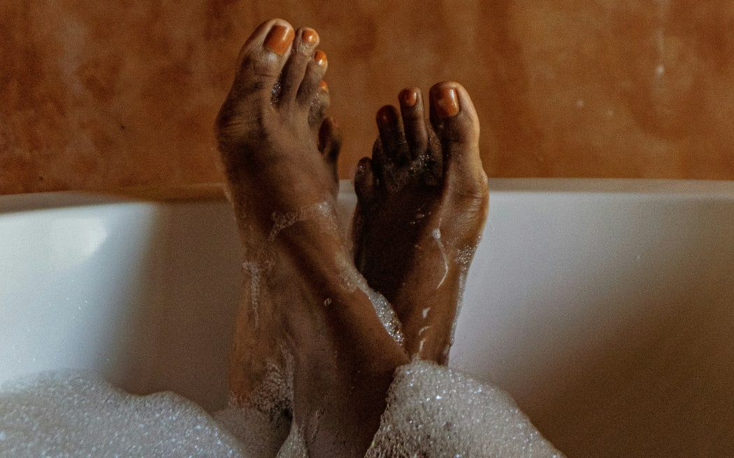 A close up of female feet painted with orange nail polish resting on the side of a bath.
