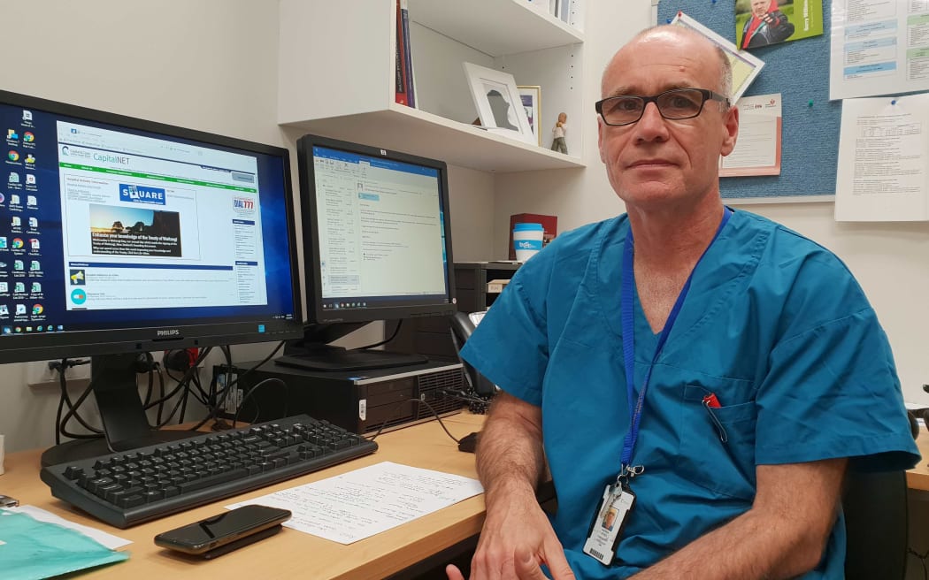 Wellington Cardiologist, Dr Andrew Aitken,  in hospital scrubs sitting in his office