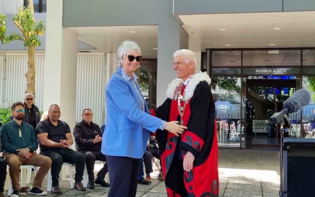 Woman in light blue jacket shakes hands with man in mayoral robs and chains