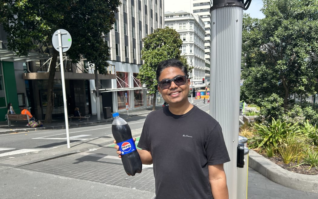A man smiling at the camera holding a bottle of soda drinks.