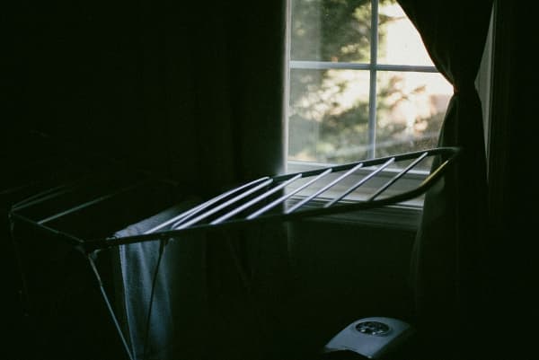 A clothes airer near a window with a little sunlight beaming through.