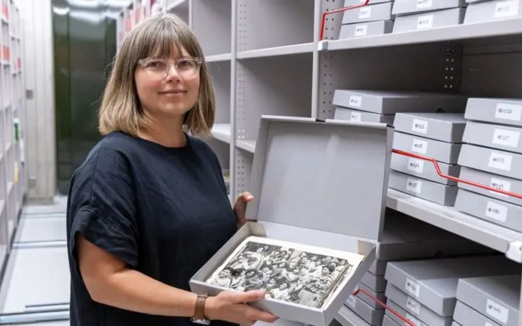 Jessica stands in an archive holding a box of photos.