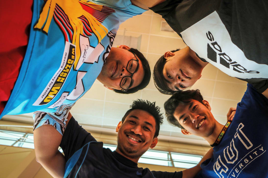 Four Asian teenagers in a huddle look down at photographer