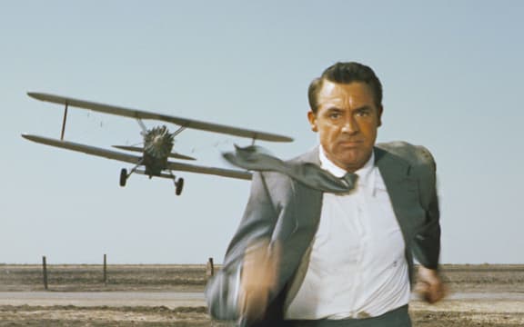 Movie still from Alfred Hitchcock's film North by Northwest featuring Cary grant being chased by a crop-dusting biplane.