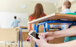 A student texting in a classroom under his desk during a lesson.