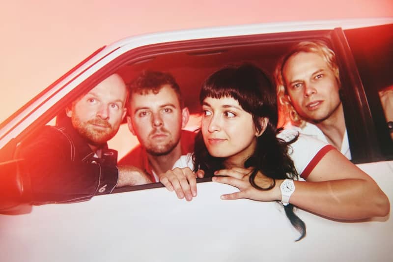 Four people in rosy light inside a white car door.