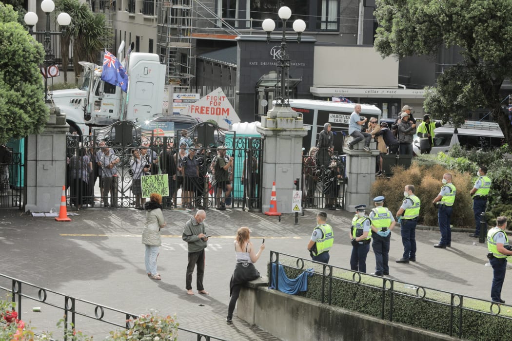 People watch on at the gates of Parliament as police make multiple arrests in an effort to remove protesters occupying the precinct for a third day.