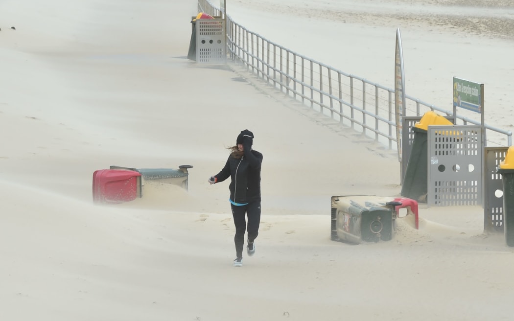 A jogger struggles against sand whipped up by strong winds at Bondi Beach in Sydney.