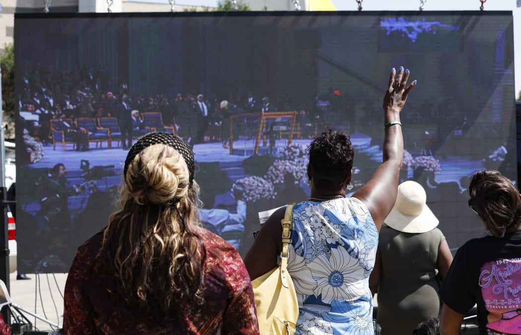 Fans watch the singer's funeral on a giant screen outside Greater Grace Temple as the singer's funeral takes place inside.