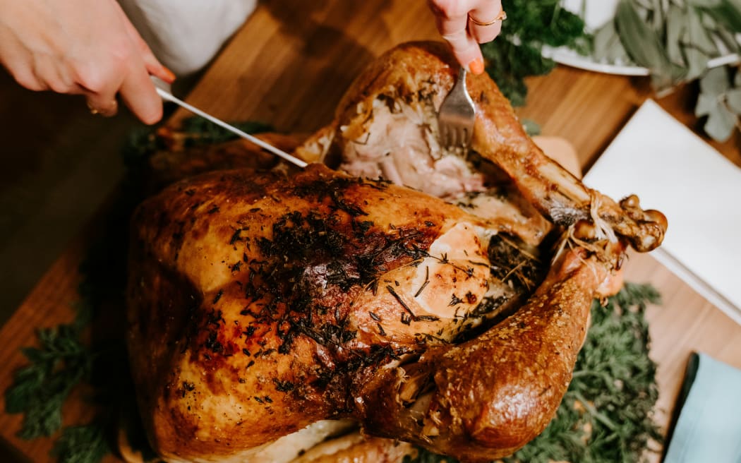 A person cuts open a cooked turkey on a dinner table.