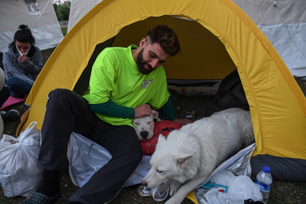 A man pets one of his dogs as he is sheltered in a tent in Izmir, on November 1, 2020 after a powerful earthquake struck Turkey's western coast and parts of Greece. -