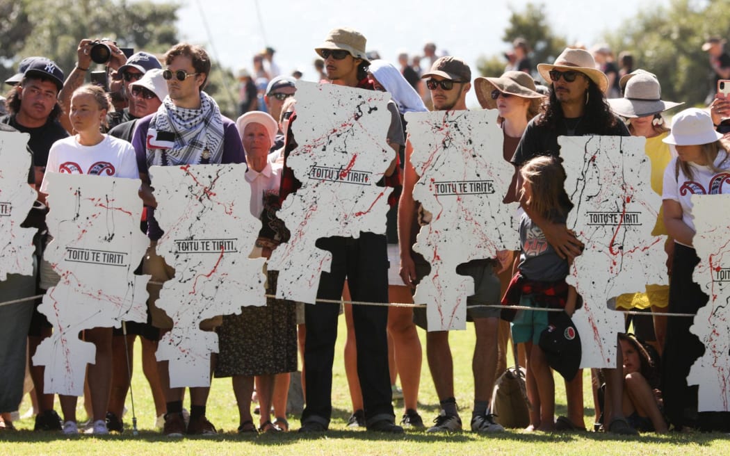 Kāhui (group) gathered at the Treaty grounds holding Toitū Te Tiriti posters as te hau kāinga prepare to welcome the government at Waitangi Monday 5 February 2024.