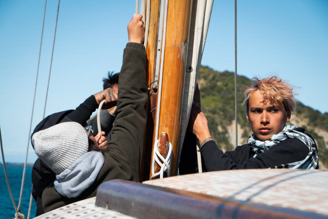 Crew members take instruction from their captain as they fasten the main sail.