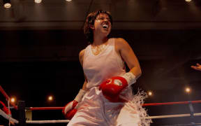 Sydney Sweeney has short dark hair and stands in a boxing ring wearing boxing gloves and a mouthguard.